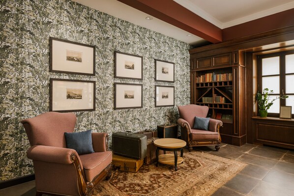 A cozy living room with two armchairs, a small round table, and a bookshelf filled with books. - Andrássy Kúria & Spa (Tarcal)