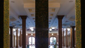 A large indoor swimming pool with a tiled floor and walls, surrounded by columns and arches. - Andrássy Kúria & Spa (Tarcal)