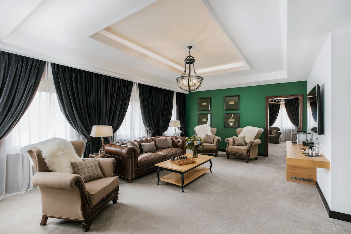 A spacious living room with a brown leather sofa, a wooden coffee table, and a green accent wall.