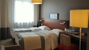 A hotel room with two beds, a wooden headboard, a desk with a lamp, a telephone, and a picture frame on the wall.