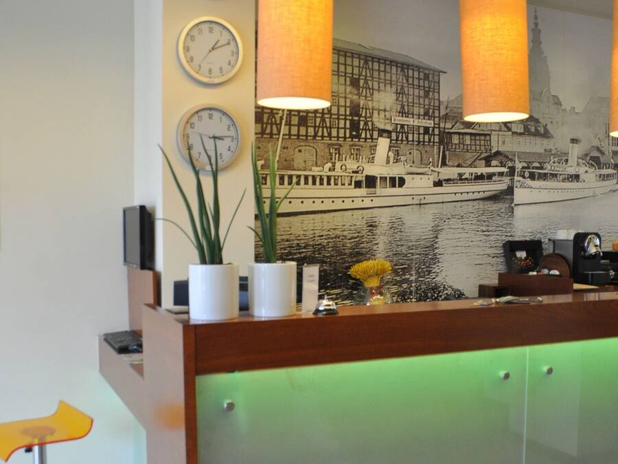 Un mostrador de recepción moderno con una sección inferior iluminada en verde, un mural de un barco en la pared y tres relojes de pared.