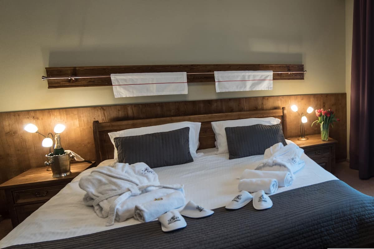 Een hotelkamer met een groot bed, twee nachtkastjes met lampen, een houten hoofdbord en uitzicht op het landschap door dunne gordijnen.