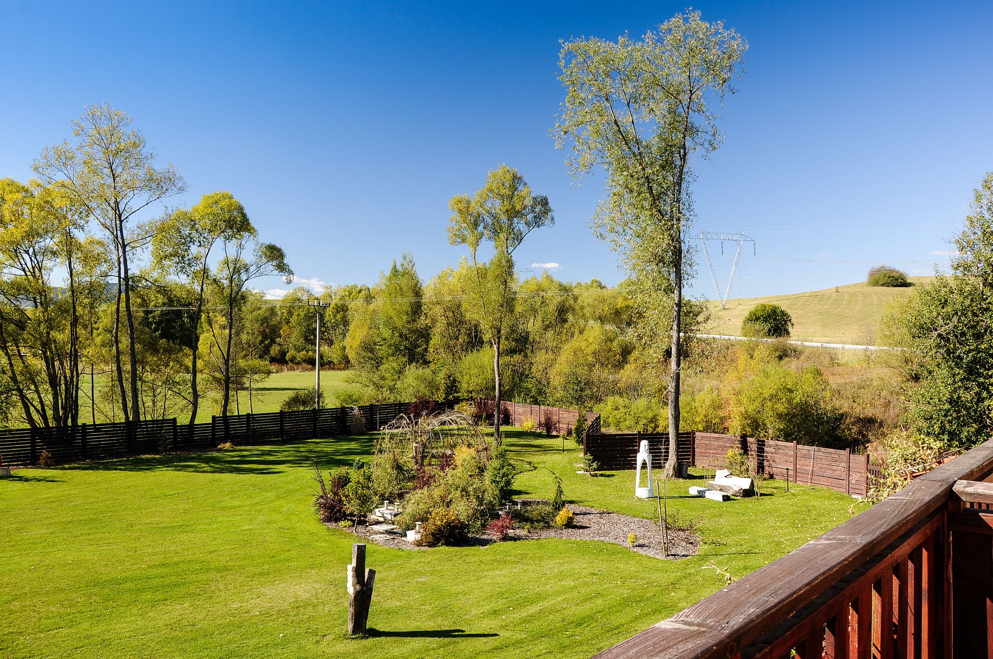 A grassy outdoor area with trees, a wooden fence, and a wooden deck.