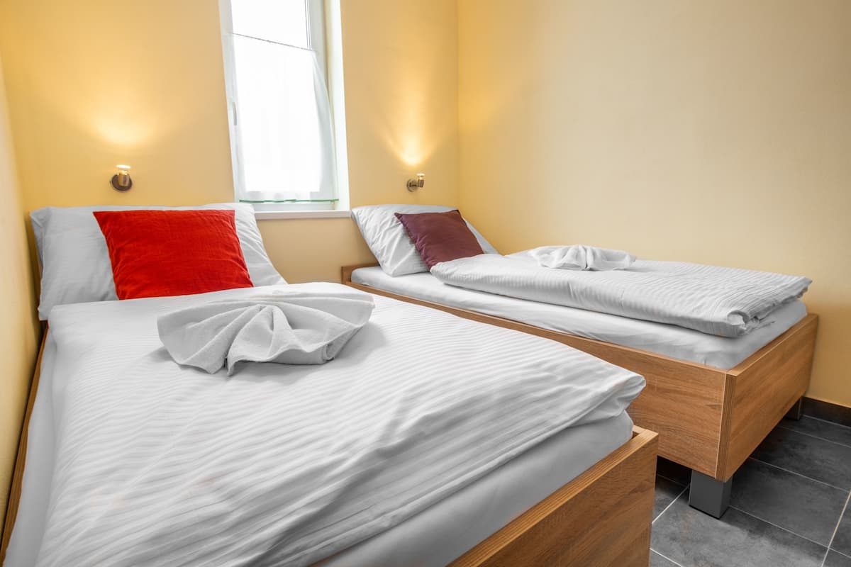 Een hotelkamer met twee bedden, elk voorzien van witte beddengoed en een rode kussen.