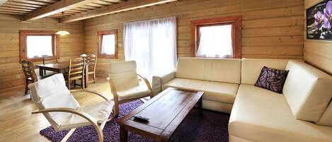 Un interior acogedor de cabaña con techo de madera, un sofá, una mesa de comedor con sillas y una ventana con cortinas.