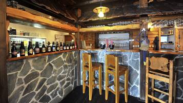 Zona de bar rústica con paredes de piedra, taburetes de madera y una variedad de botellas y vasos.