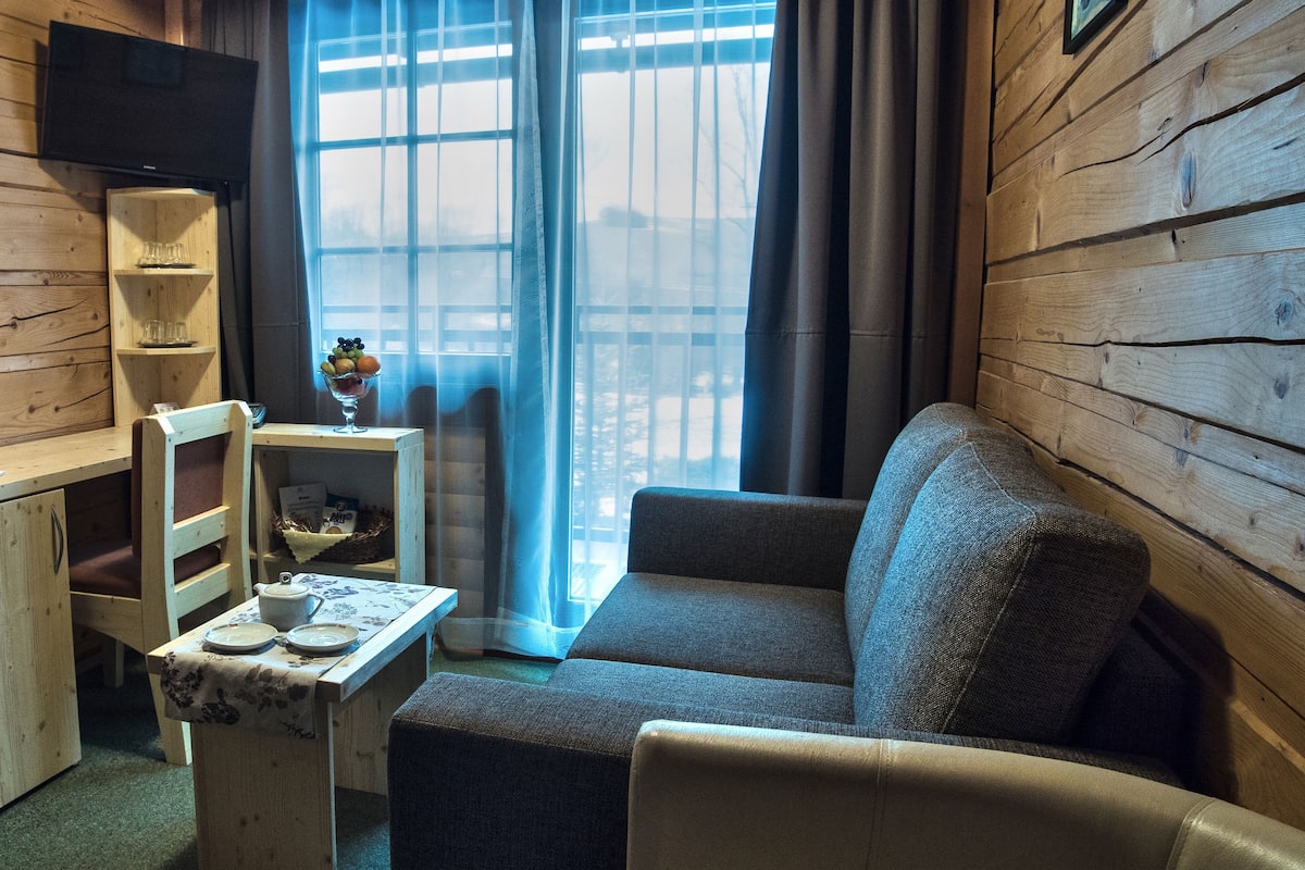 Een gezellige kamer met houten inrichting, een bank, een klein tafeltje met theeservies en een raam met gordijnen.