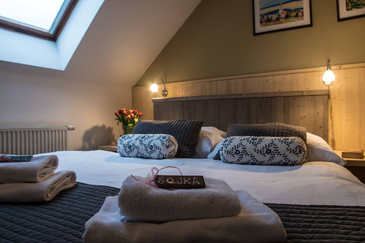 Een net opgemaakt bed met een naambordje, een gewatteerd sprei en een dakvenster erboven.