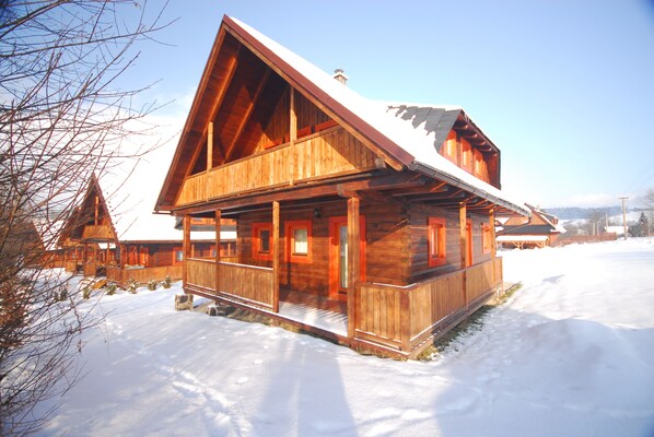 A wooden cabin with a sloped roof, a balcony, and a snow-covered ground.