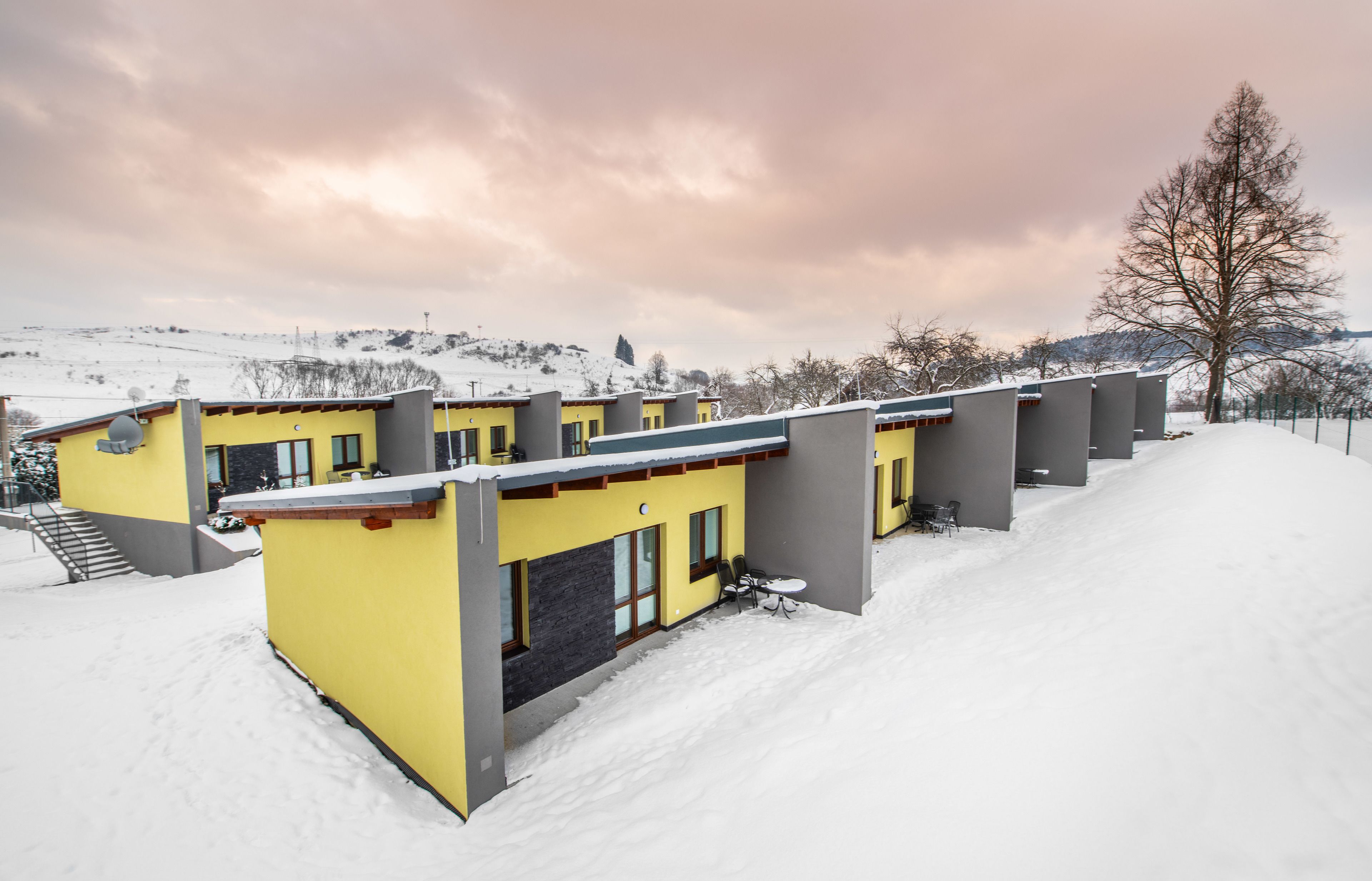 Eine Reihe gelber Gebäude vor einer verschneiten Landschaft und einem bewölkten Himmel.