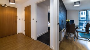 A hotel room with wooden flooring, a dining area with a table and chairs, and a view of the outside through a window. - Comfort Zone Serviced Apartments (Birmingham)