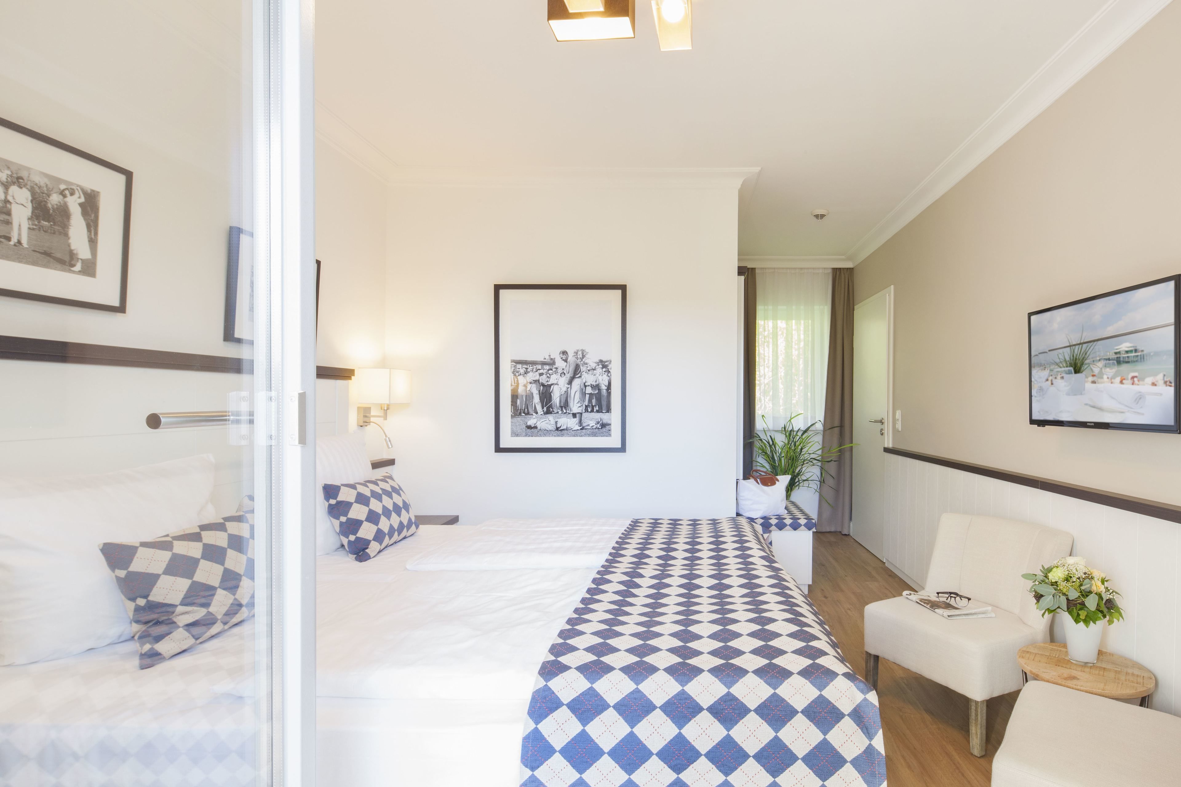 Et hotelværelse med seng, skrivebord, stol og et lille bord med en plante.