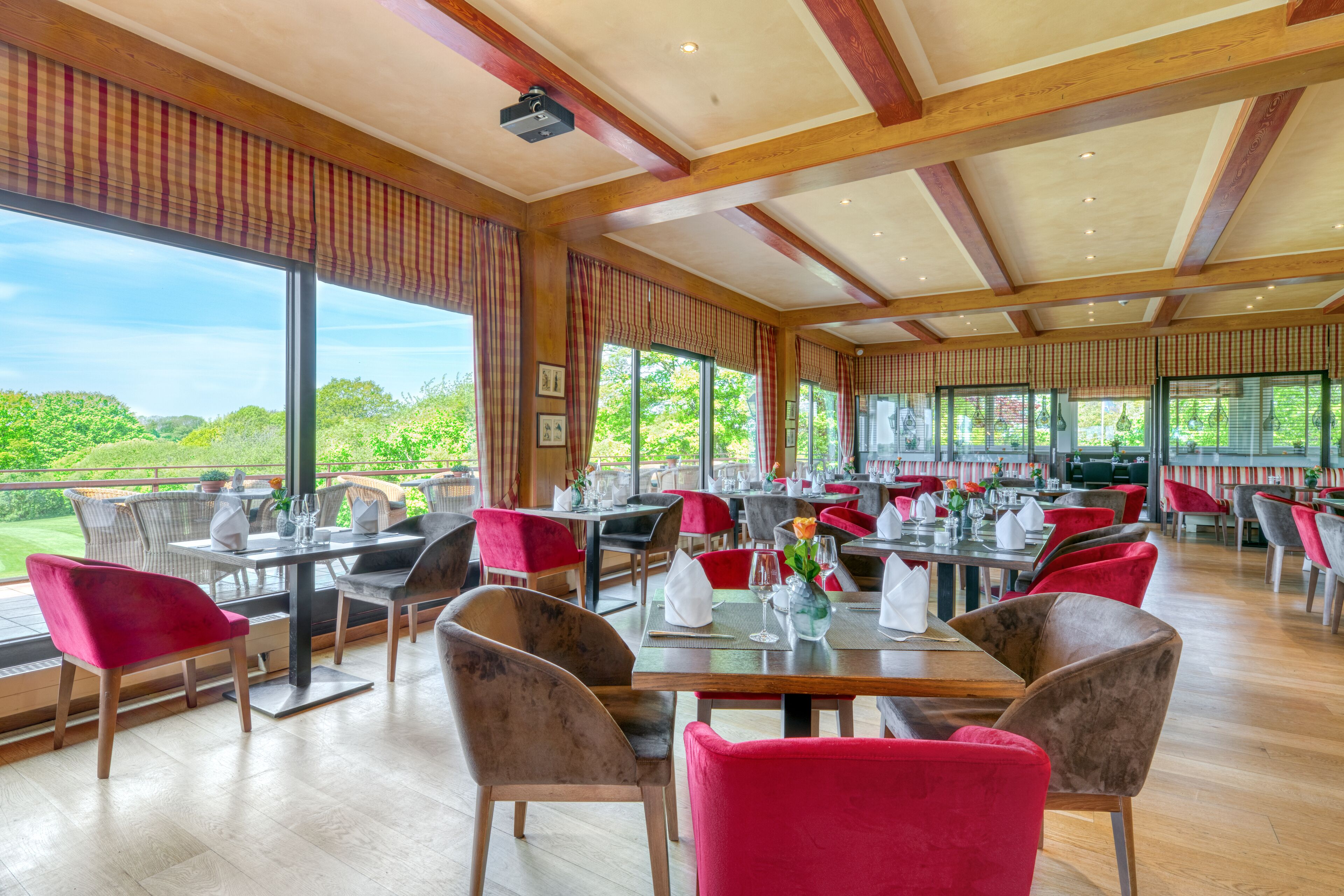 A spacious dining area with wooden beams, large windows, and red chairs.