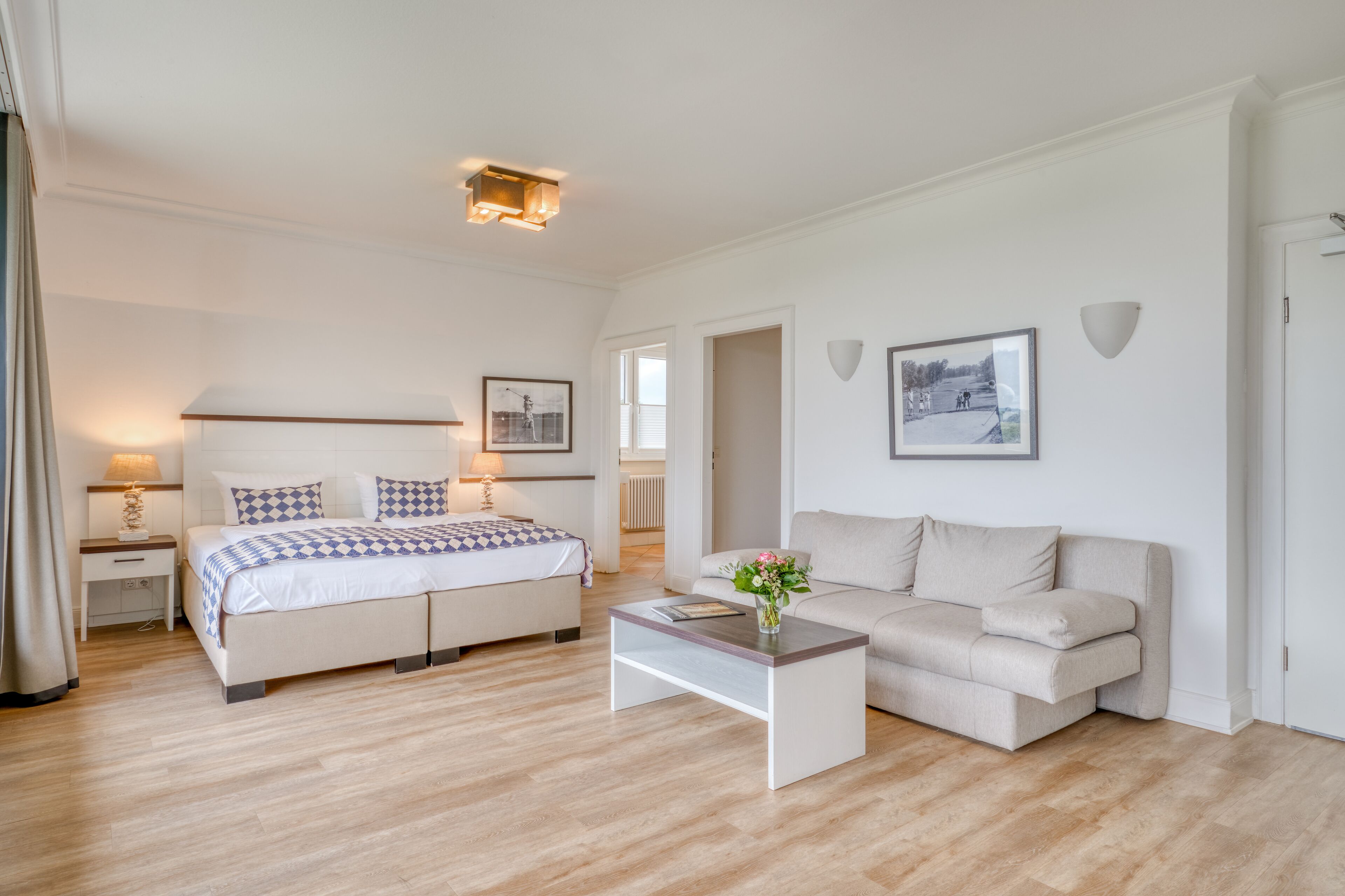 Een moderne hotelkamer met een tweepersoonsbed, een slaapbank, een bijzettafeltje en een klein bureau met lamp.