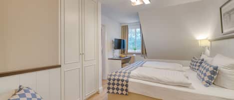 A bedroom with two beds, a desk, a TV, and a window with curtains.