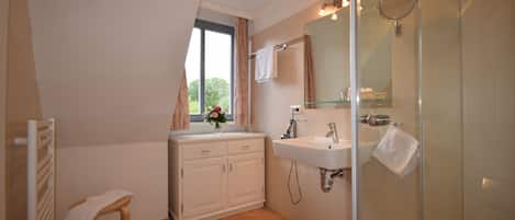A bathroom with a shower, a sink, a mirror, and a window with curtains.