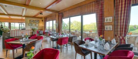 Ein geräumiges Restaurant mit Holzbalken, rot gepolsterten Stühlen und großen Fenstern mit Blick ins Freie.