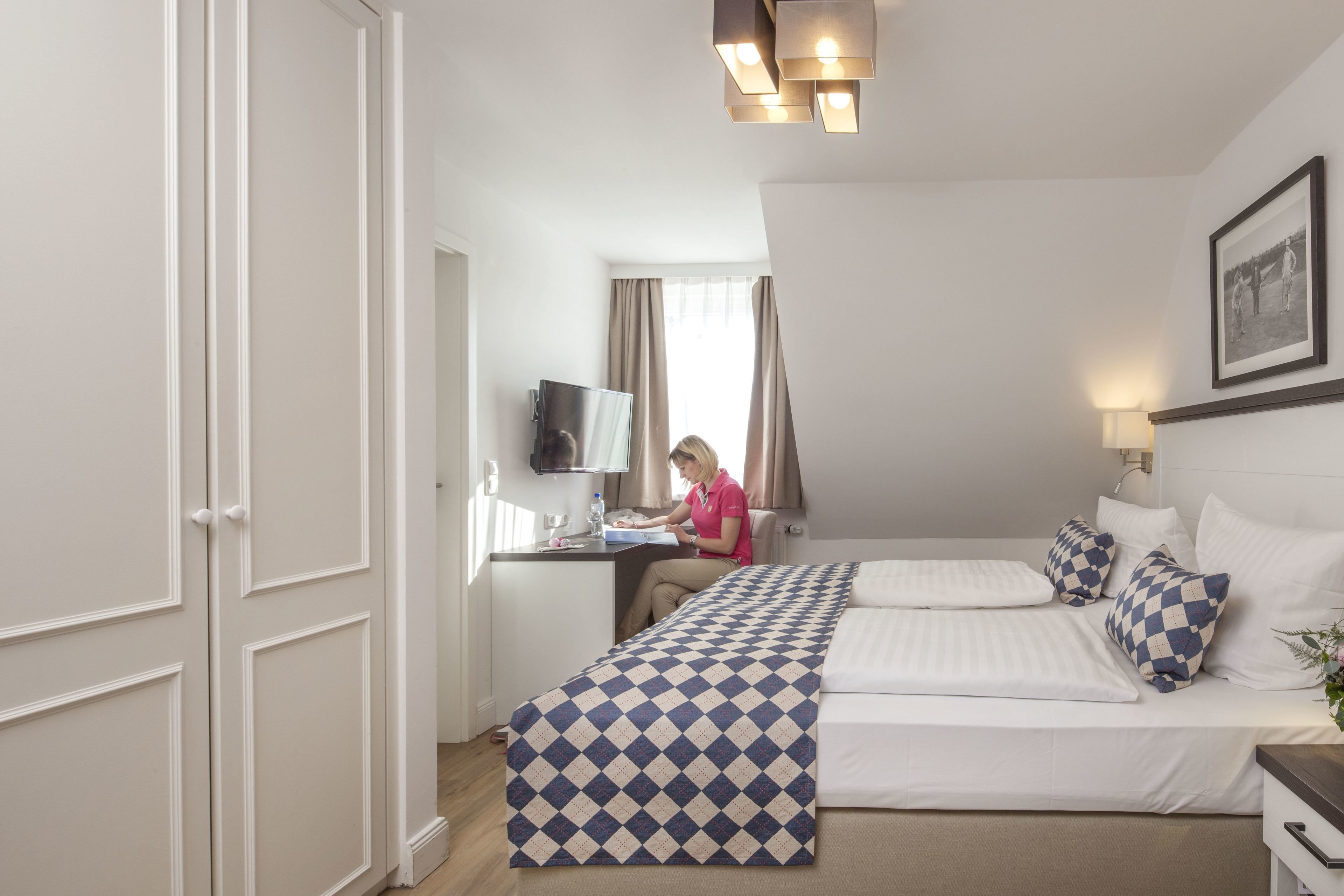 Ein Hotelzimmer mit Bett, Schreibtisch mit Computer, Fernseher und einem Fenster mit Vorhängen.