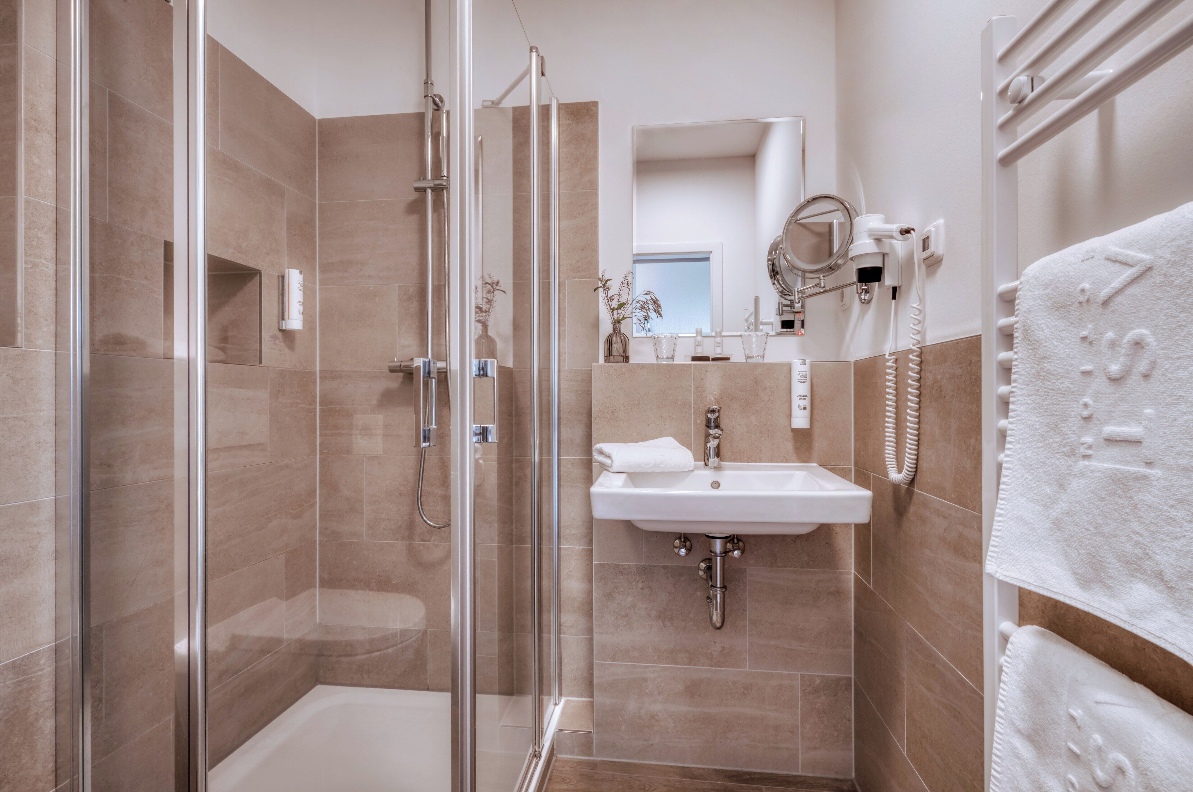 A modern bathroom with a glass-enclosed shower, a sink, and a towel rack.
