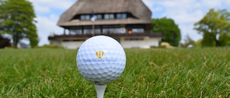 A golf ball on a tee on a grassy field with a building in the background.