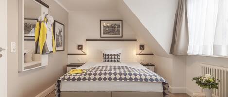 Un dormitorio con una cama grande, un espejo, un cuadro en la pared y una mesita de noche con un florero.
