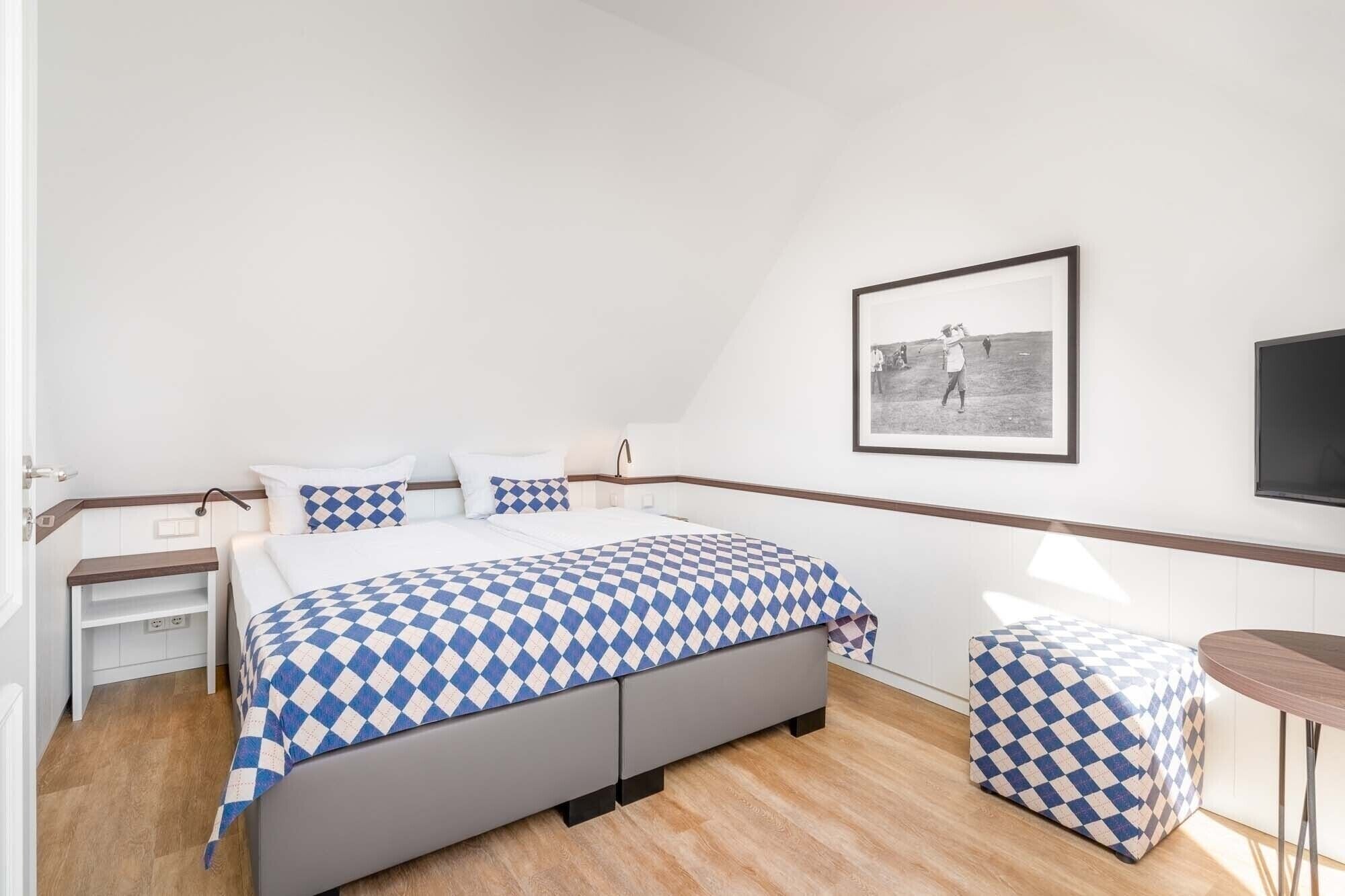 A bedroom with a bed, bedside tables, a small stool, a framed picture on the wall, and a television.