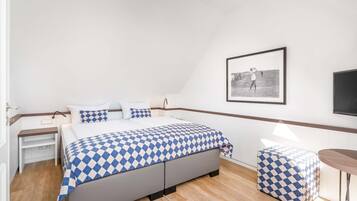 A bedroom with a bed, bedside tables, a small stool, a framed picture on the wall, and a television.