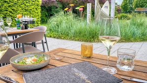 An outdoor dining area with a wooden table, a bowl of salad, a glass of white wine, and a candle. - Strandgrün Golf- & Spa Resort (Timmendorfer Strand)
