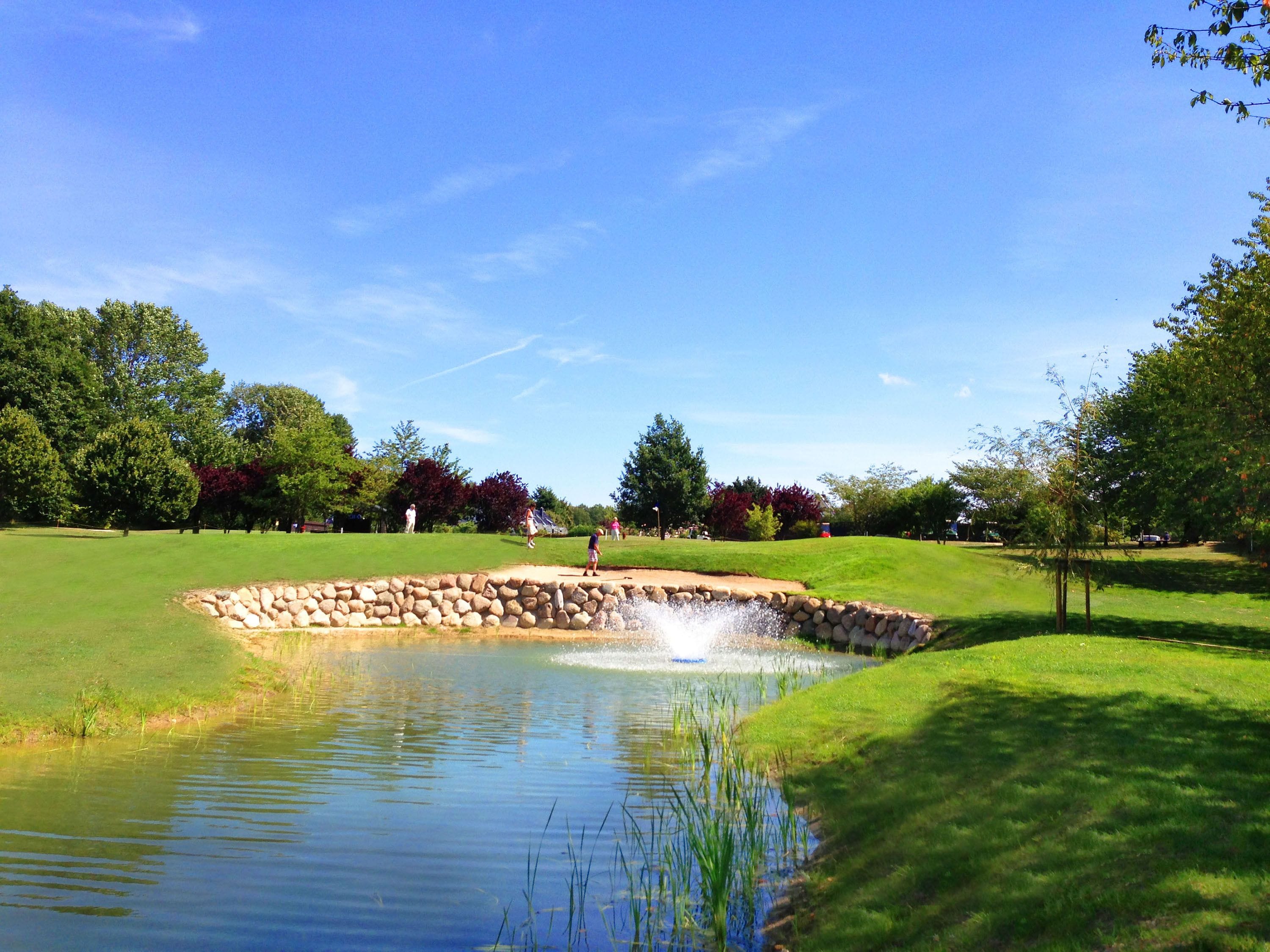 Un campo de golf con un estanque, muros de piedra y árboles.