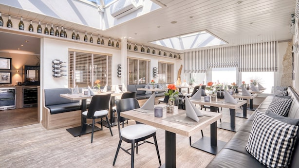 A modern dining area with high ceilings, skylights, and a variety of seating options including tables, chairs, and sofas. - Strandgrün Golf- & Spa Resort (Timmendorfer Strand)