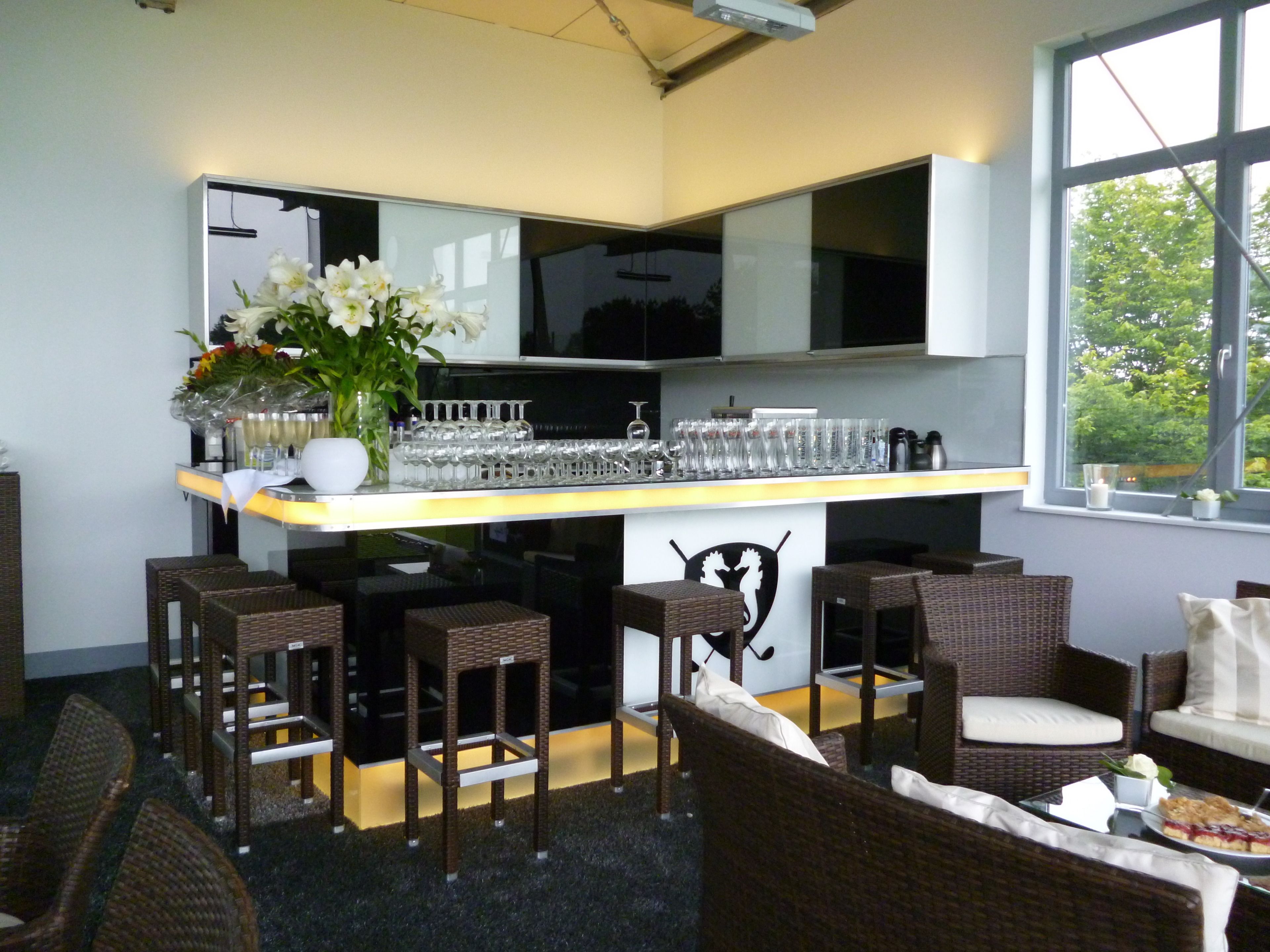 A bar area with wicker furniture, a white countertop, and a large window with a view of trees.