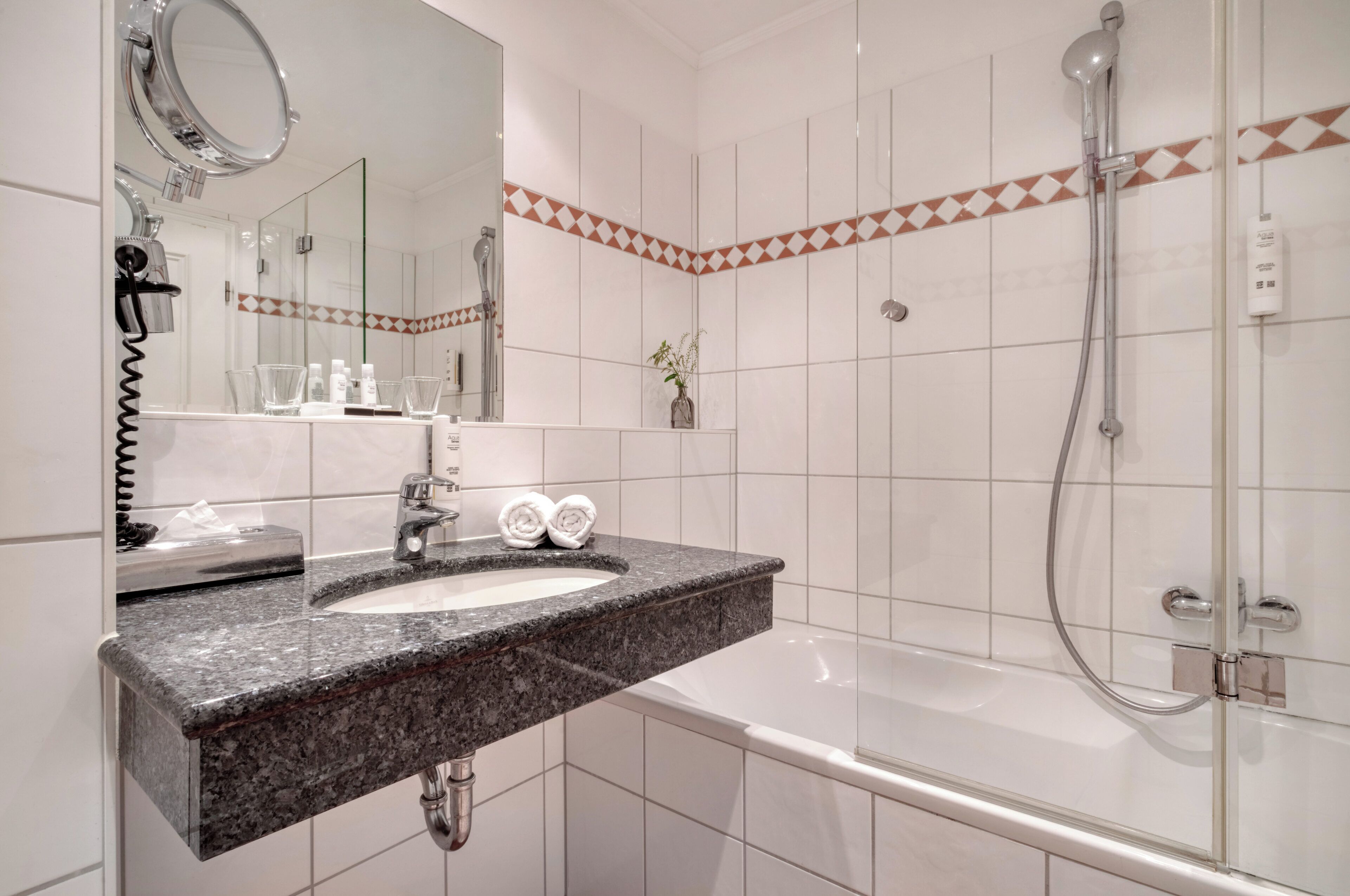 A modern bathroom with a granite countertop, a white sink, a mirror, a shower, and a towel rack.