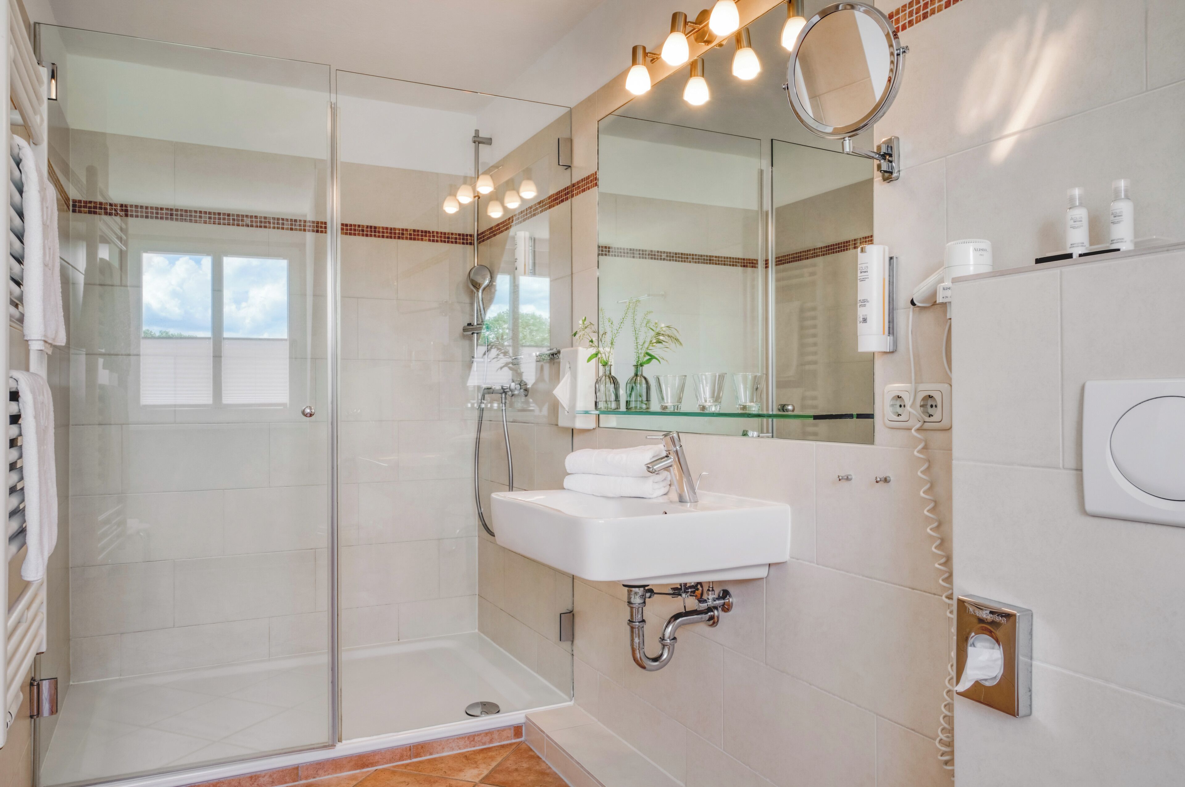 A modern bathroom with a glass-enclosed shower, a white sink, and a large mirror with lights.
