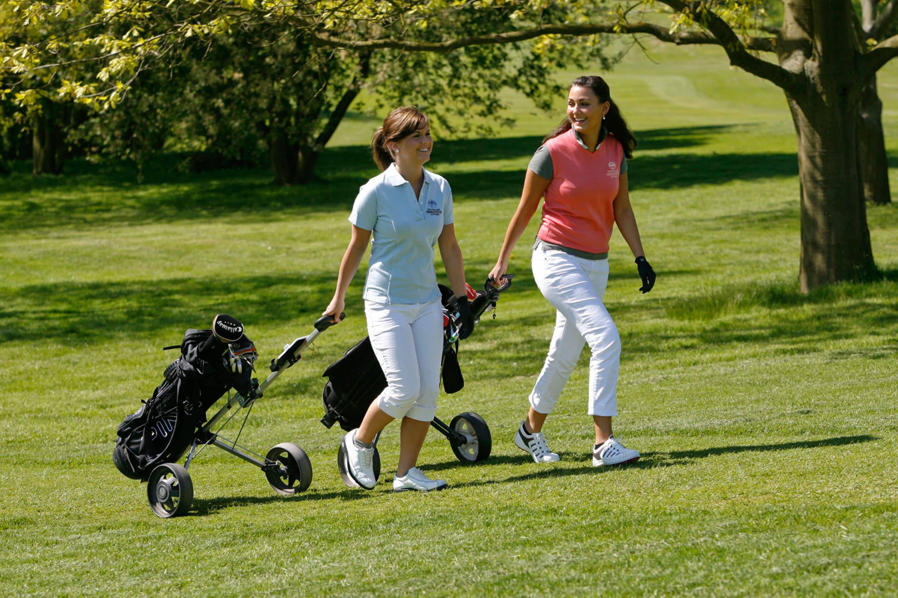 Two people walking on a grassy field with a golf bag and a golf cart.