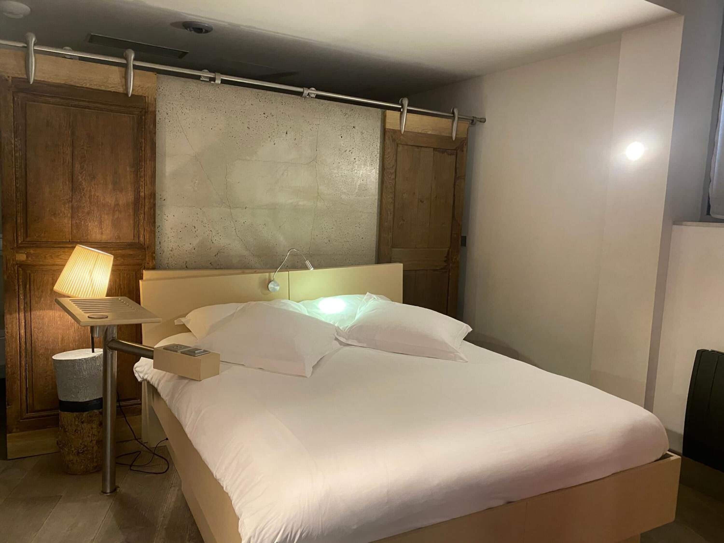 Un lit avec du linge de lit blanc, une table de chevet avec une lampe et une tête de lit en bois.
