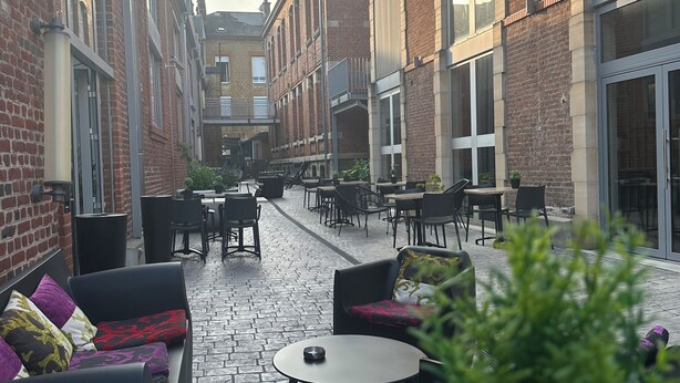 A courtyard with outdoor seating, a potted plant, and brick buildings.