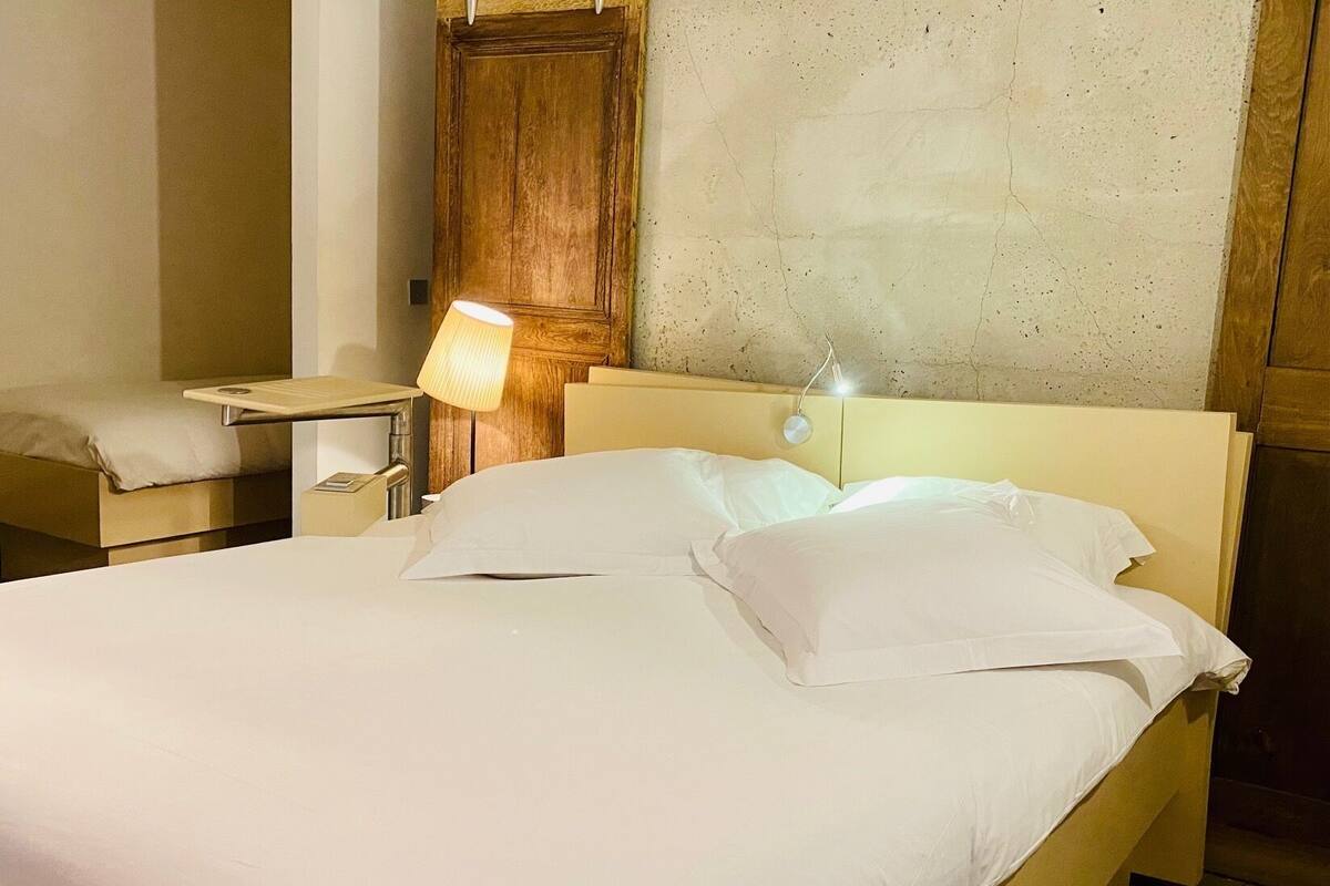 A single bed with white linens in a room with a wooden headboard and a nightstand with a lamp.