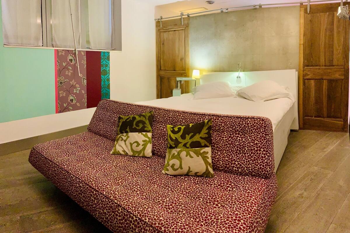 A bedroom with a bed, a sofa, and a wooden wardrobe.