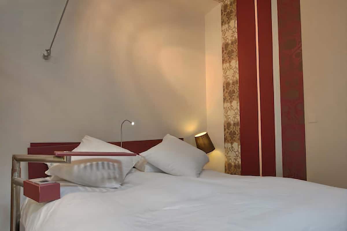 A neatly made bed with white linens, a red headboard, and a bedside table with a lamp.