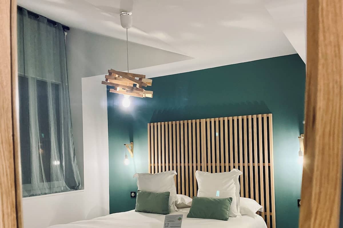 A modern bedroom with a bed, wooden headboard, and a hanging light fixture.