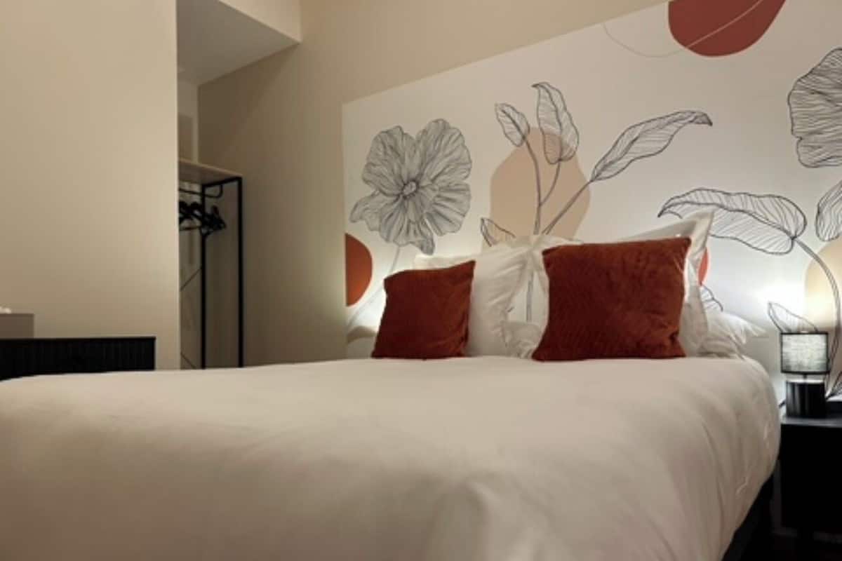 A hotel room with a large bed, a nightstand with a lamp, and a wall with floral artwork.