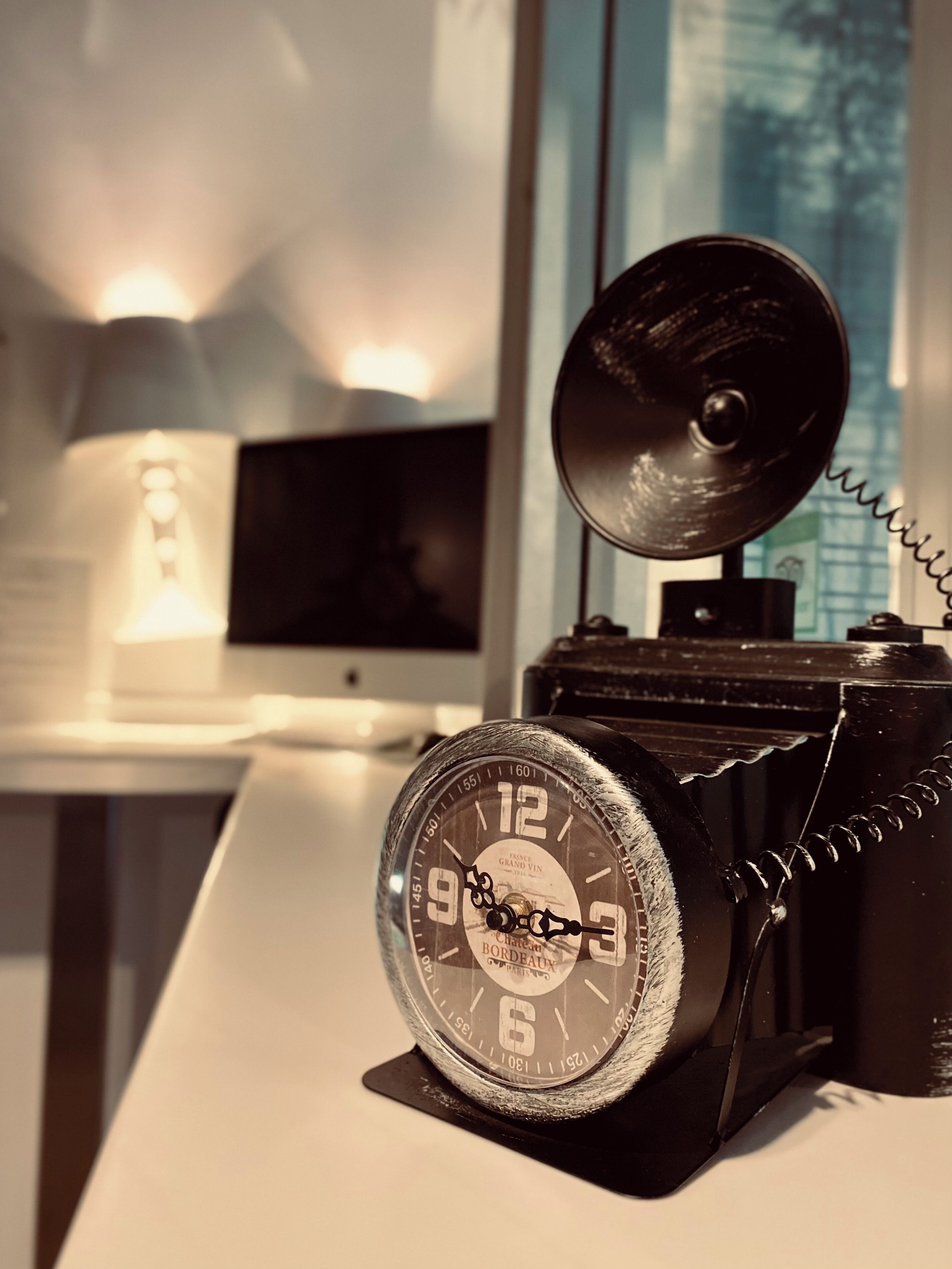 A vintage telephone with a clock, a lamp, and a television in the background.