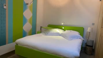 Un lit bien fait, avec du linge de lit blanc, dans une chambre dont la tête de lit est verte et dont le mur est décoré de motifs rayés.
