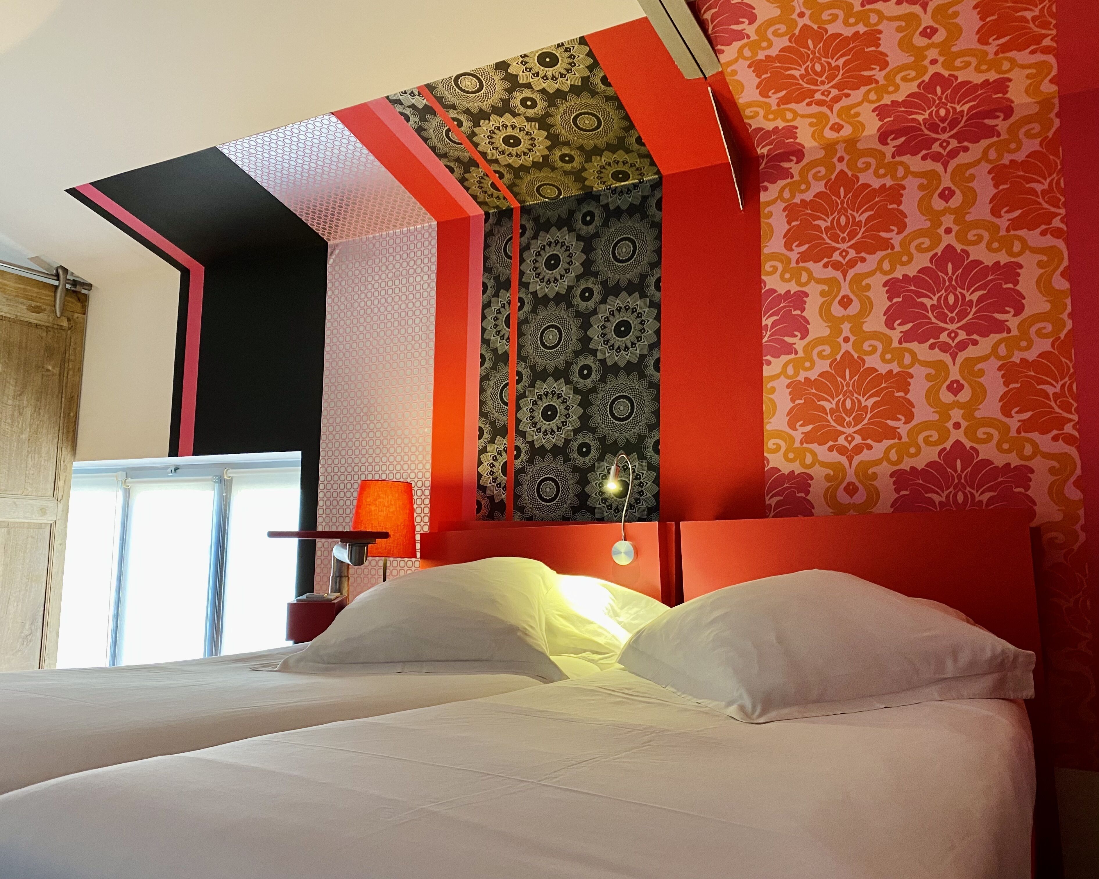 Un lit avec du linge de lit blanc, une tête de lit rouge et un mur à motifs derrière.
