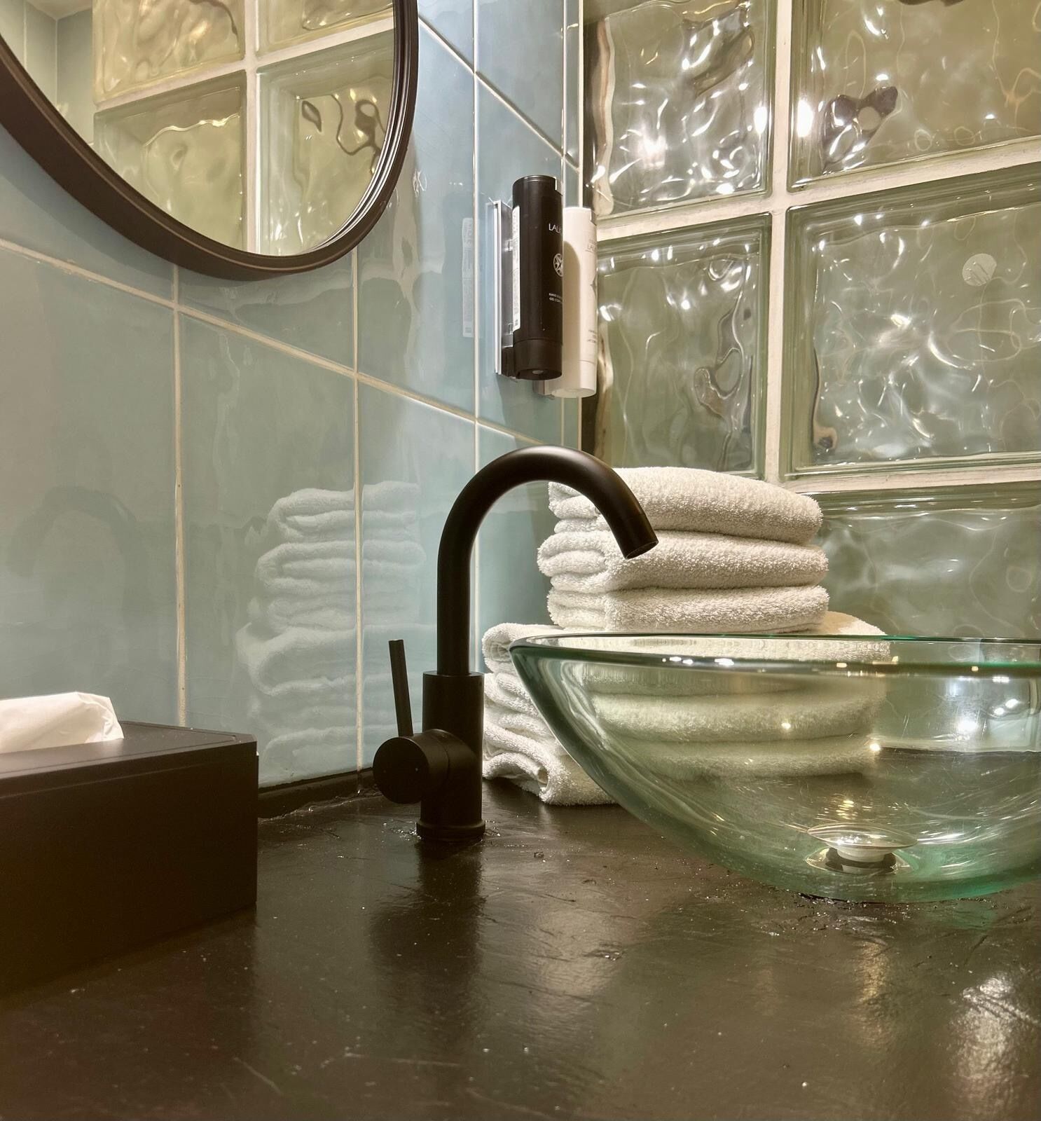 Ein Badezimmer mit einem schwarzen Wasserhahn, einer Waschschüssel aus Glas und einem Handtuchhalter mit gefalteten Handtüchern.