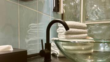 Ein Badezimmer mit einem schwarzen Wasserhahn, einer Waschschüssel aus Glas und einem Handtuchhalter mit gefalteten Handtüchern.