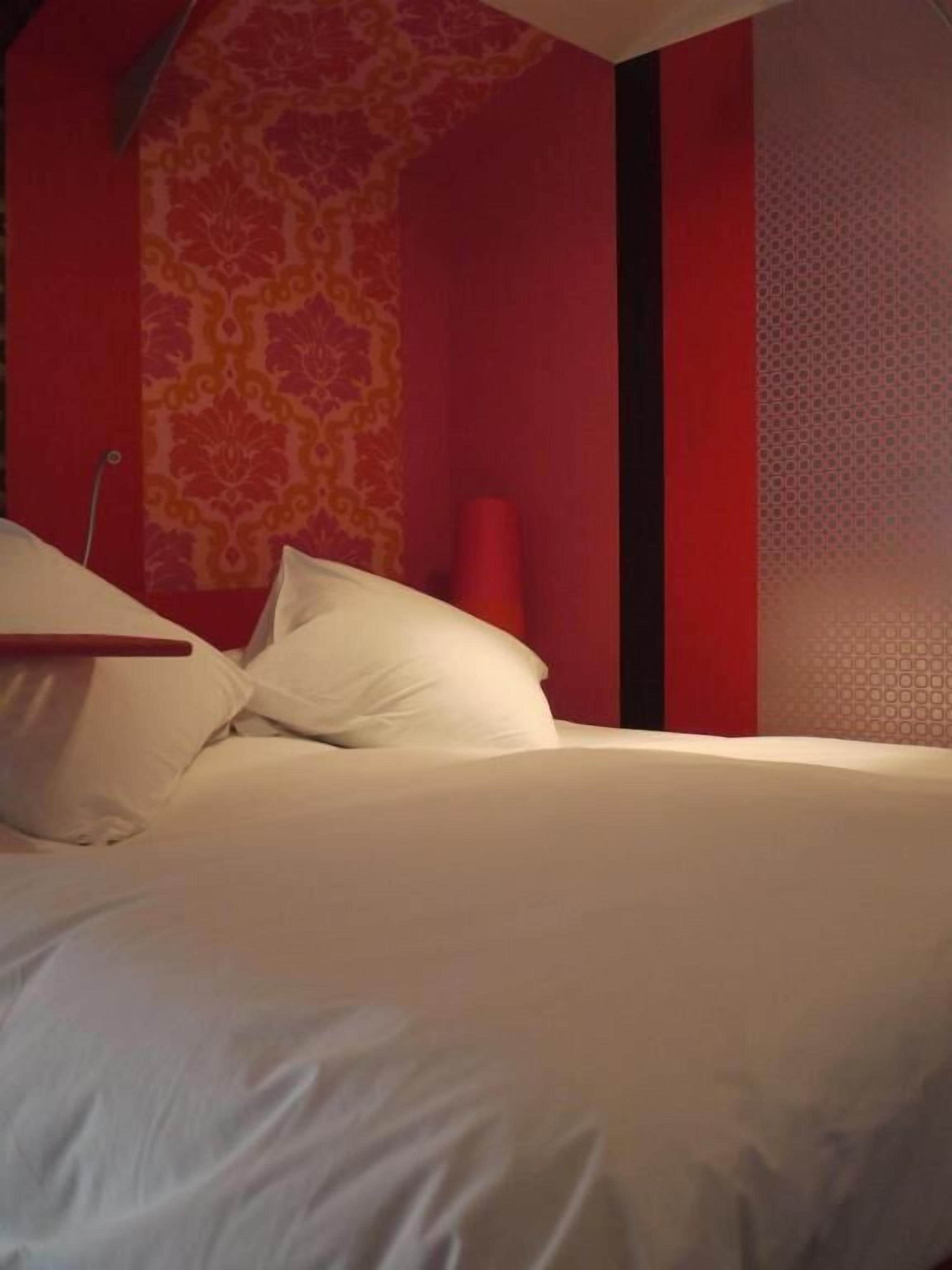 A bed with white linens in a room with red walls and a patterned wallpaper.