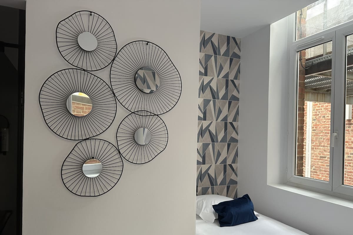 A bedroom with a bed, a window, and a wall with geometric patterned tiles.