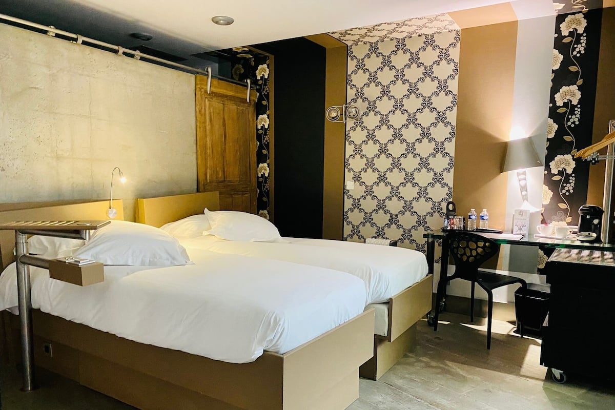 A hotel room with two beds, a desk, a chair, and a wardrobe.