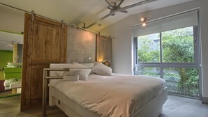 A modern bedroom with a large bed, wooden paneling, a ceiling fan, and a large window with a view of greenery.